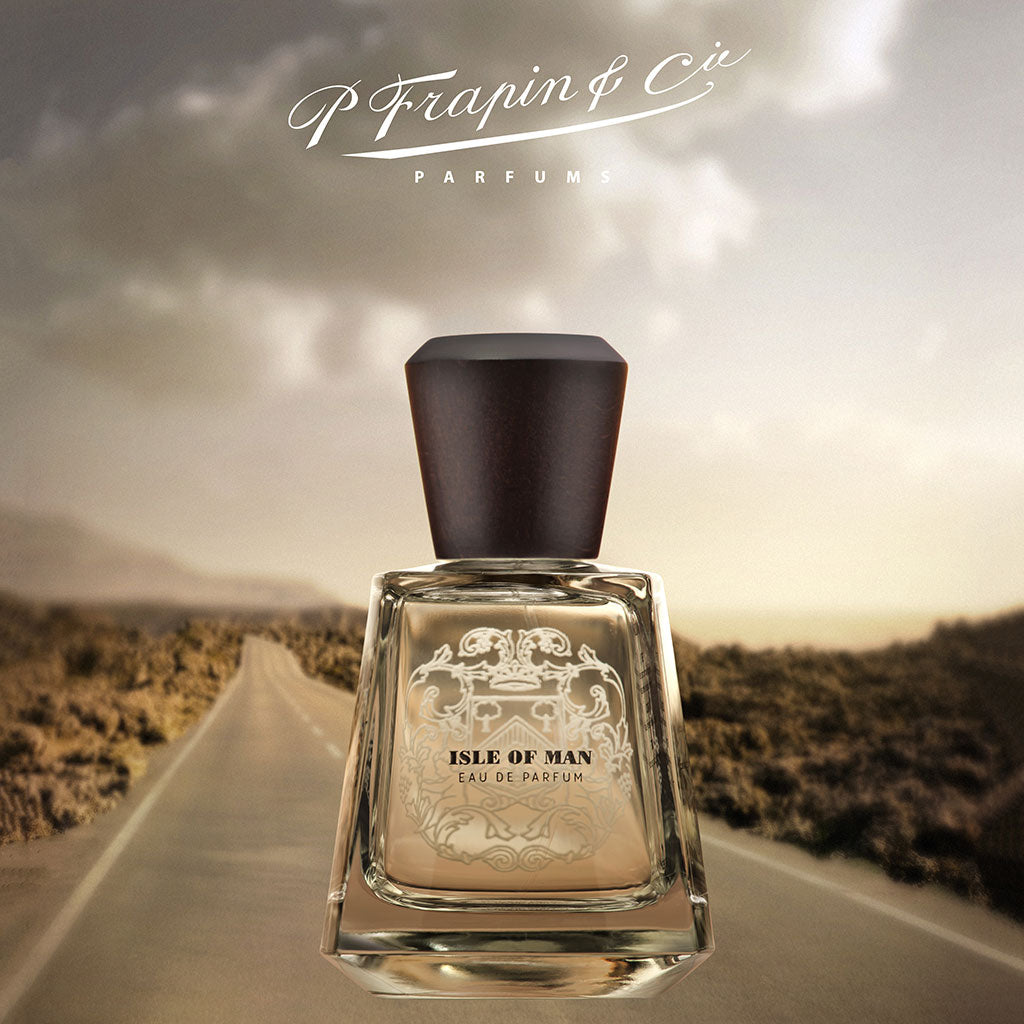 Isle of Man Eau de Parfum by Frapin, 100ml bottle displayed outdoors with a sunset and countryside background